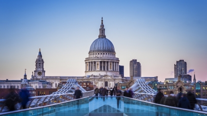 Londoners walking through Millennium Bridge with St.Paul's Cathedral at the background after sunset - London, UK