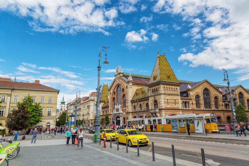 BUDAPEST, HUNGARY - MAY 2017: Central Market Hall in Budapest city, Hungary, Europe. Pedestrian crossing and yellow tram, taxi in foreground, old building and blue sky in background.