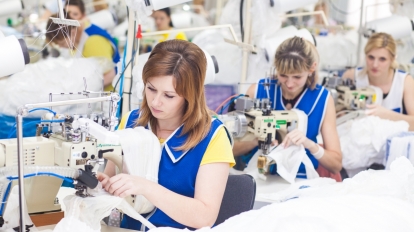 GRODNO BELARUS - DECEMBER 13 2013: Seamstress in textile factory sewing with a industrial sewing machine .