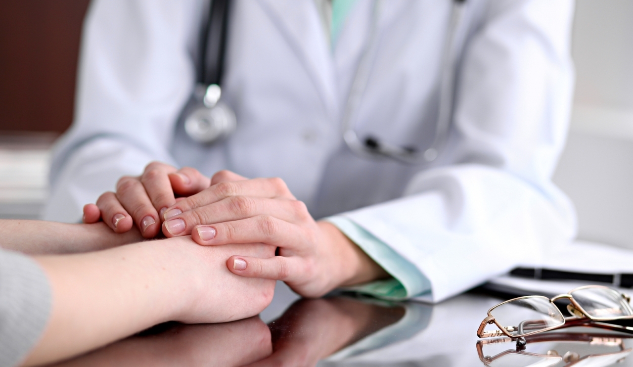 Friendly female doctor hands holding patient hand sitting at the desk for encouragement, empathy, cheering and support while medical examination. Bad news lessening, compassion, trust and ethics concept