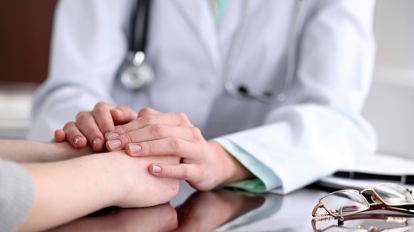 Friendly female doctor hands holding patient hand sitting at the desk for encouragement, empathy, cheering and support while medical examination. Bad news lessening, compassion, trust and ethics concept