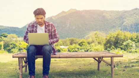 Young man working on his laptop connect to wireless internet in rural area. Internet connection allows people to work anywhere from laptop. Notebook and nature background. Wireless technology concept.