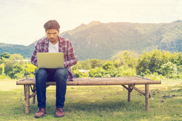 Young man working on his laptop connect to wireless internet in rural area. Internet connection allows people to work anywhere from laptop. Notebook and nature background. Wireless technology concept.